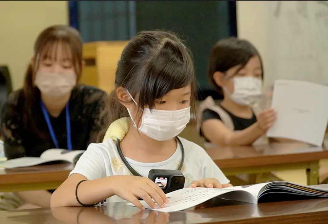 机に広げた教材を読む児童。読み手の大人とともに教材を確かめている様子