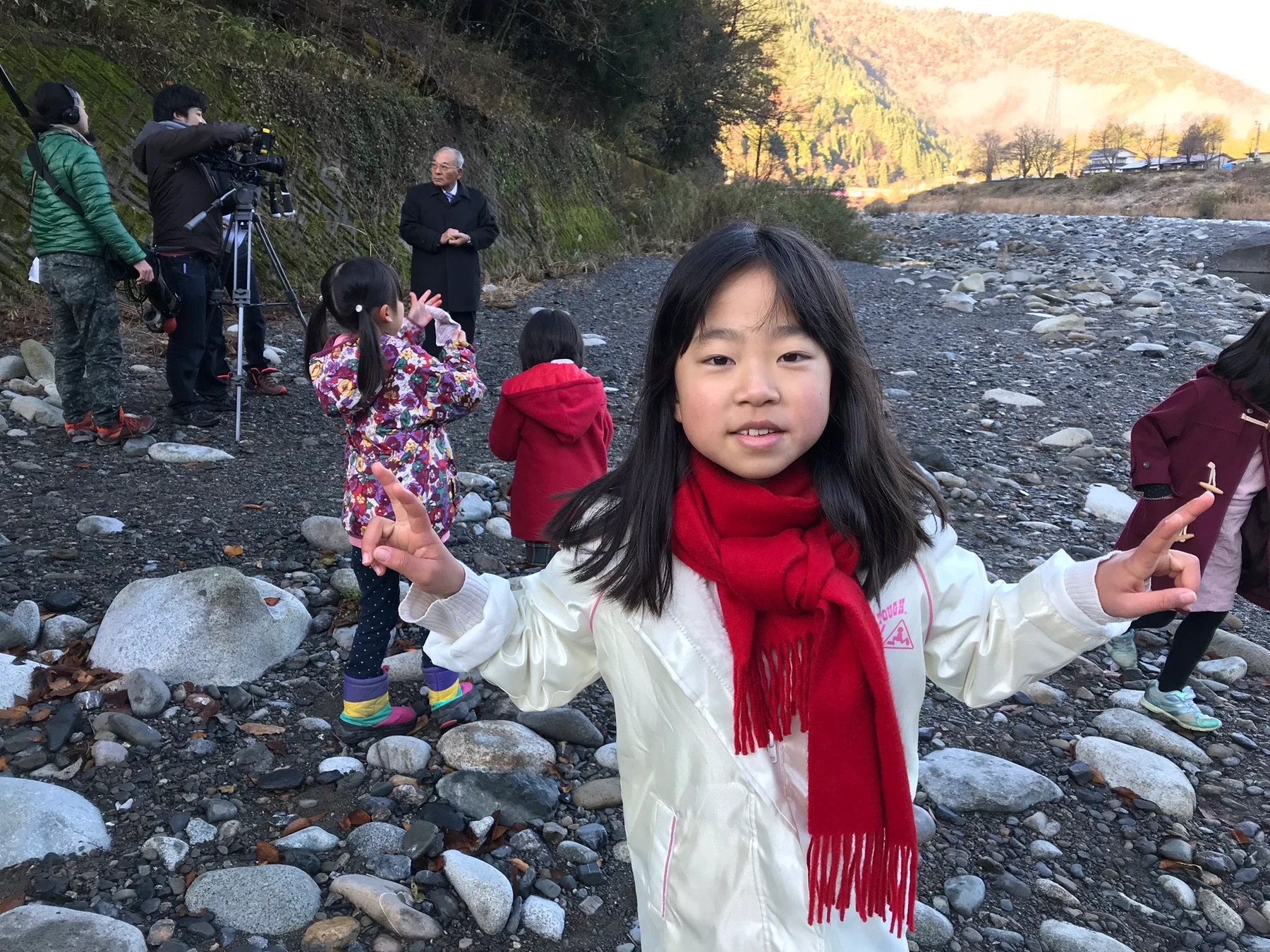 河原でカメラを構える撮影スタッフと、子どもたちを含む出演者